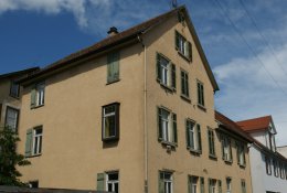 Ockerfarbenes Mehrfamilien-Eckhaus mit schmutzig-grünen Fensterläden