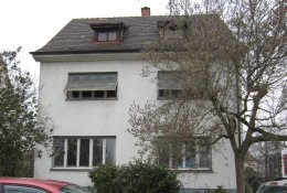 Weiß gestrichenes Gebäude von Traufseite mit vier großen, länglichen Fenstern; zwei kleine Gauben im bräunlichen Dach