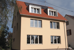 Ocker gestrichenes Gebäude von Traufseite mit vier großen, länglichen Fenstern; zwei vergrößerte Gauben im rötlichen Dach