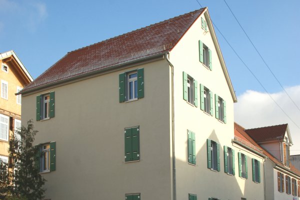 Elfenbeinfarbenes Mehrfamilien-Eckhaus mit grünen Fensterläden, die teilweise geschlossen sind