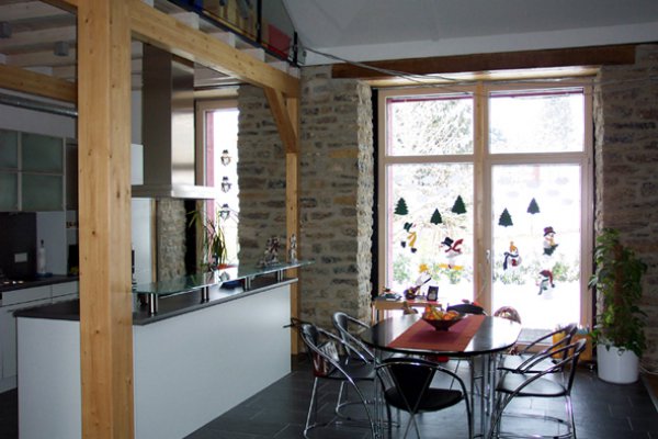 Raum mit Natursteinwänden, die großes Fenster einfassen; davor ein Tisch, links Küchenzeile